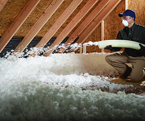 Worker installing blown-in insulation in an attic.
