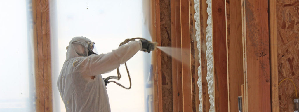 Worker in protective suit installing spray foam insulation in a wall.