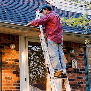 Man on a ladder cleaning out home gutters.