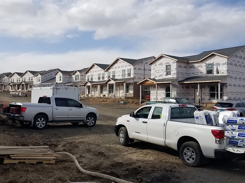 White pickup trucks carrying insulation parked in front of a row of new residential homes in Little Rock, Arkansas.