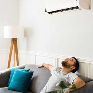 man cooling off on couch, under air conditioning mini-split on wall.
