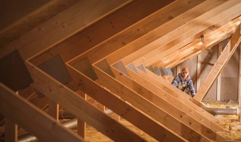 Construction Worker Insulating Attic Space Of Home.