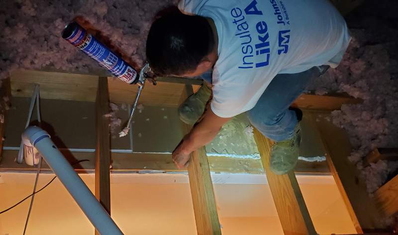 A G&S Insulating professional air sealing a residential attic floor using a professional-grade spray foam sealant to prevent air leaks before adding blown-in insulation.