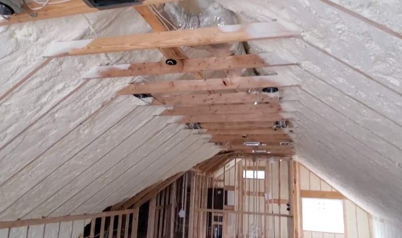 Professional installation of open-cell spray foam insulation between wooden rafters in a residential attic by G&S Insulating.