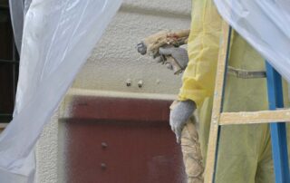 G&S Insulating technician on ladder spraying closed cell spray foam on exterior of plastic-wrapped storage container in Little Rock, AR.
