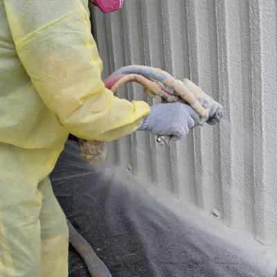 Technician in protective coveralls applying spray foam insulation to a wall for G&S Insulating in Little Rock, AR.