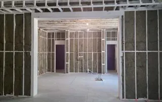 G&S Insulating rock wool batt insulation in wall framing seen through a wide framed opening into adjoining rooms in Little Rock, AR.